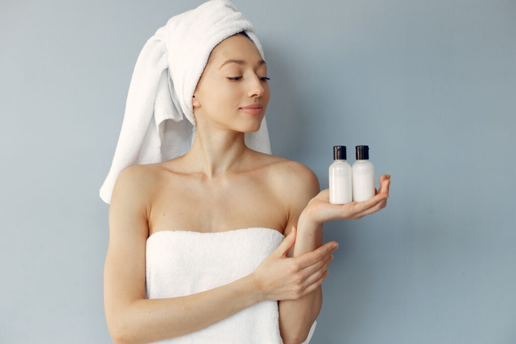 Mulher com toalha na cabeça e dois frascos de body splash na mão